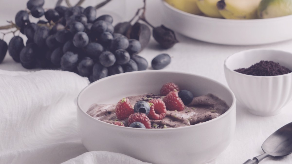 Un bol de crema de frutos rojos con frambuesas y arándanos, con uvas y plátanos al fondo