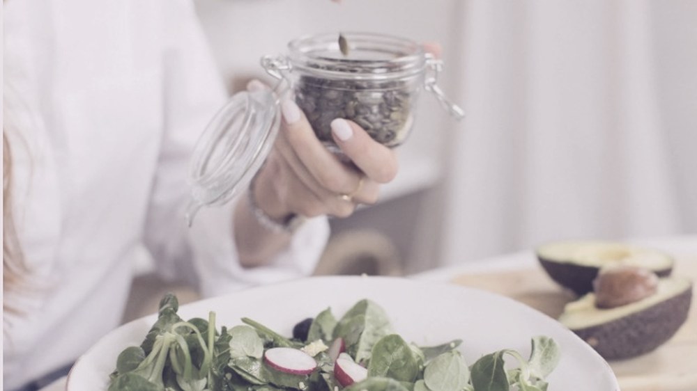 Una mujer añade semillas a un bol de ensalada con rabanitos y aguacate